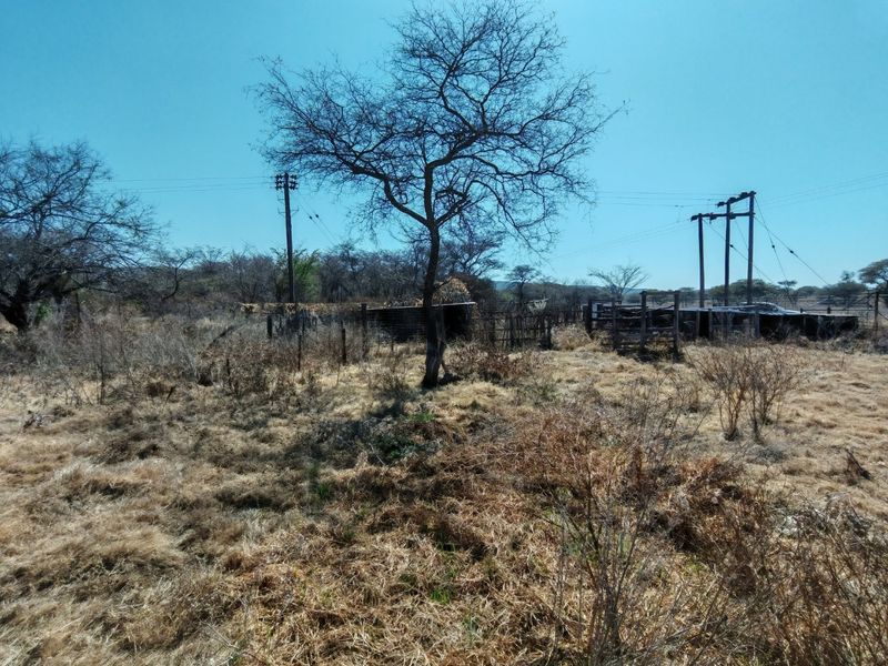 A view of vacant residential land featuring dry vegetation, utility poles with overhead power lines, and remnants of old wire fencing and livestock enclosures.