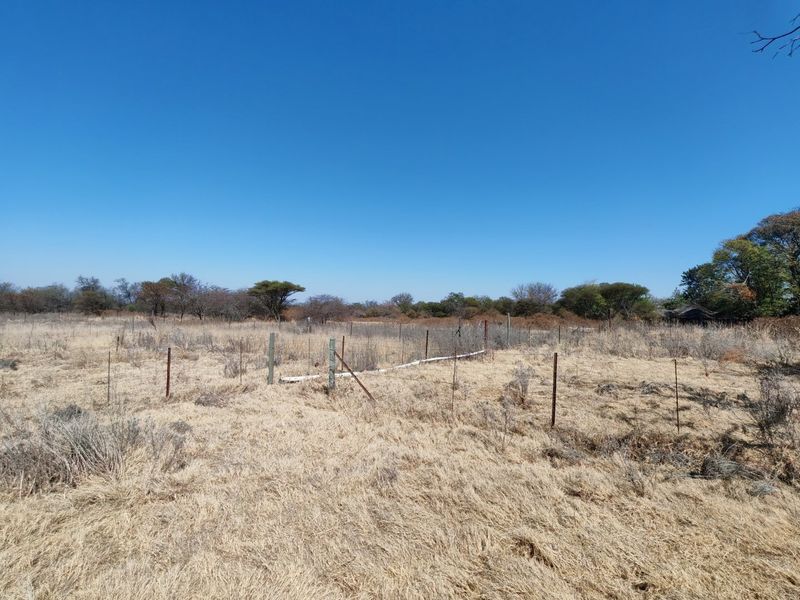 A view of a vacant residential plot featuring dry vegetation and existing wire perimeter fencing.