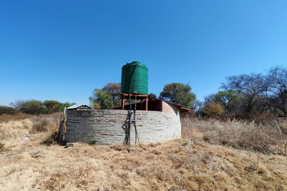 A circular brick utility structure featuring an elevated green water storage tank and associated plumbing infrastructure on a vacant residential plot.