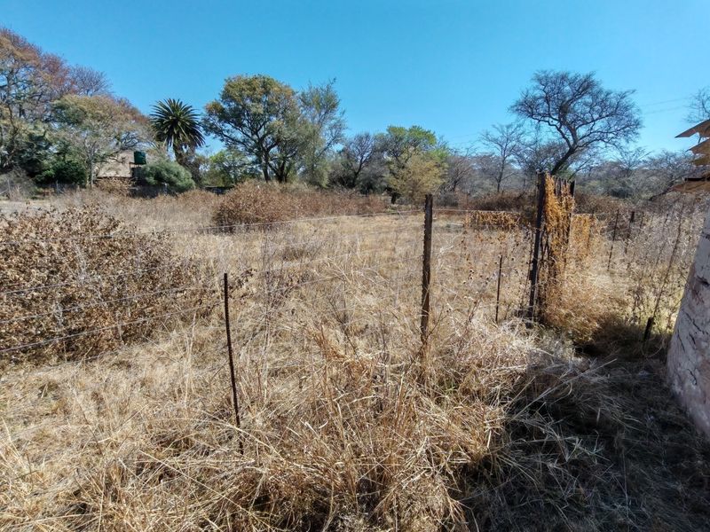 A view of a vacant residential plot featuring dry, overgrown vegetation and existing wire perimeter fencing.