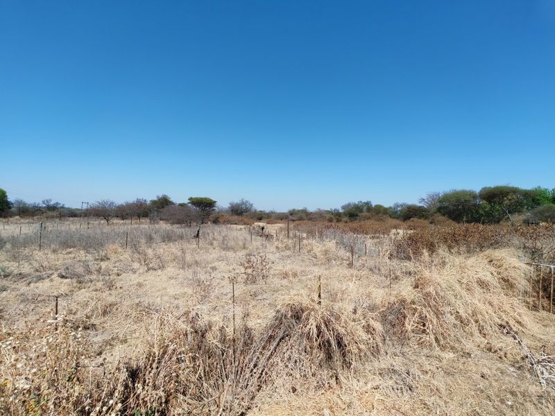 A view of a vacant residential plot featuring dry natural vegetation and perimeter wire fencing.