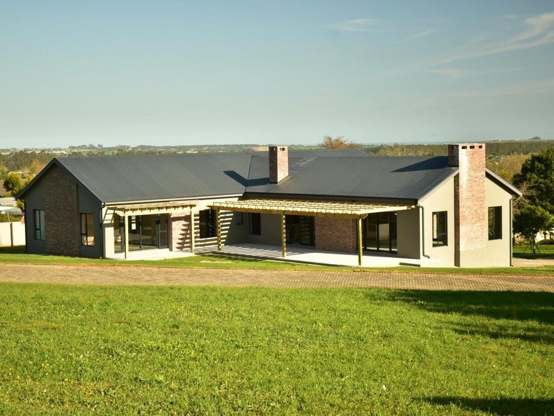 A well-maintained single-story residence featuring a metal roof, brick chimneys, and a spacious timber-framed patio area overlooking a large lawn.