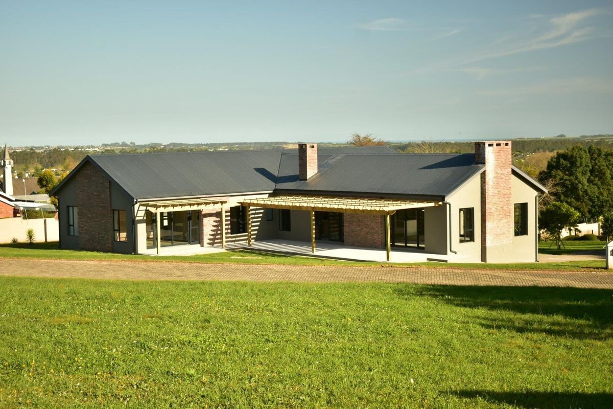 A well-maintained single-story residence featuring a metal roof, brick chimneys, and a spacious timber-framed patio area overlooking a large lawn.