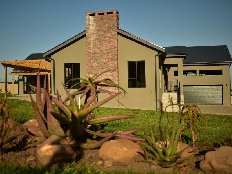 Rear view of a modern house featuring a prominent brick chimney, timber pergola, and attached garage with a well-maintained lawn.