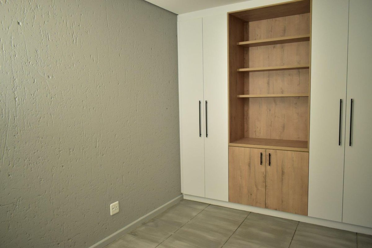 A clean, modern bedroom featuring neutral textured walls, tiled flooring, and extensive built-in cabinetry with integrated shelving and storage.