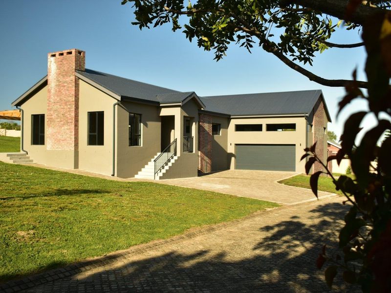 A modern single-story house featuring a brick chimney, metal roof, paved driveway, and an integrated garage, set within a well-maintained garden.