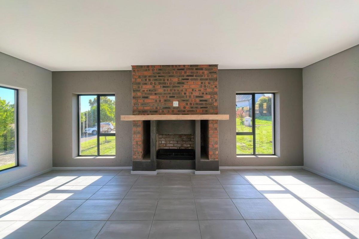Spacious living room featuring a prominent exposed brick fireplace with a timber mantelpiece, large windows, and neutral tiled flooring.