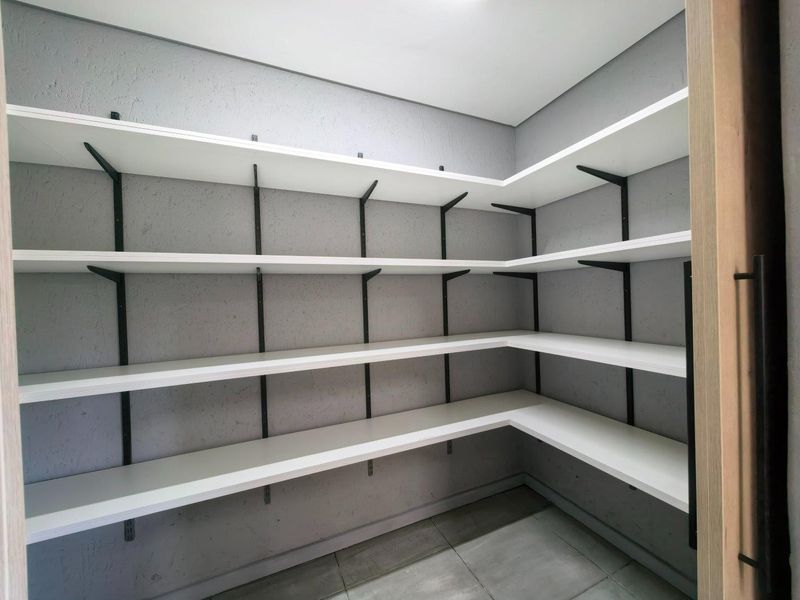 A clean, modern walk-in pantry or scullery featuring extensive built-in white shelving and neutral tiled flooring.