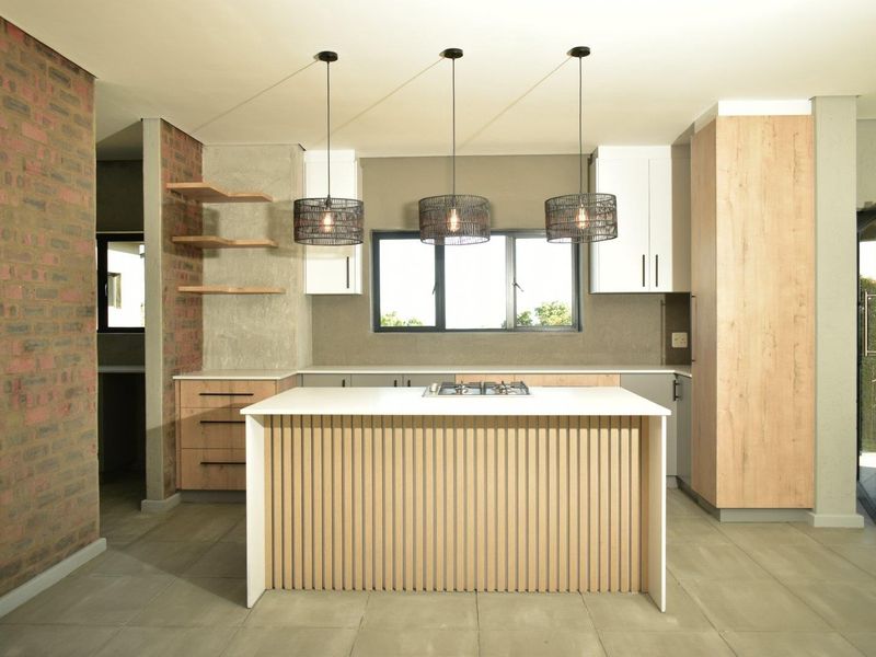 Modern kitchen featuring a central island with a gas cooktop, light wood cabinetry, exposed brick accents, and contemporary pendant lighting.