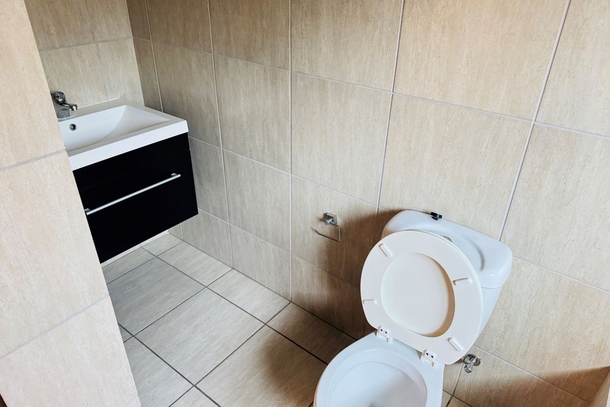 A clean, modern bathroom featuring a wall-mounted vanity with a basin and a standard toilet, finished with neutral floor-to-ceiling wall tiles.