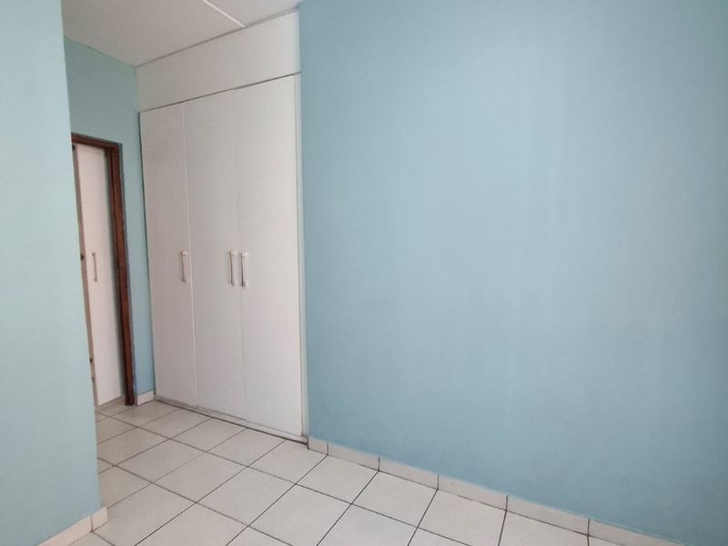 An empty bedroom featuring light blue walls, white tiled flooring, and built-in storage cupboards.