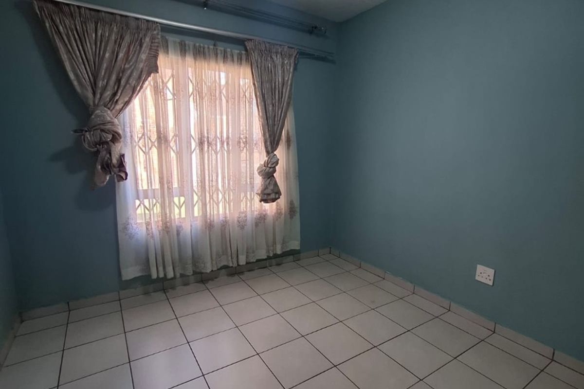 An empty bedroom featuring neutral ceramic floor tiles, blue painted walls, and a security gate on the window.