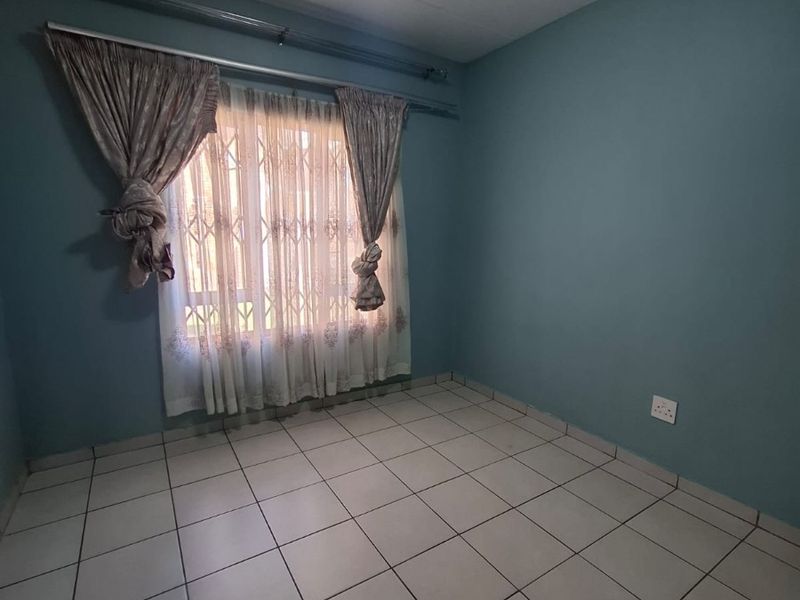 An empty bedroom featuring neutral ceramic floor tiles, blue painted walls, and a security gate on the window.