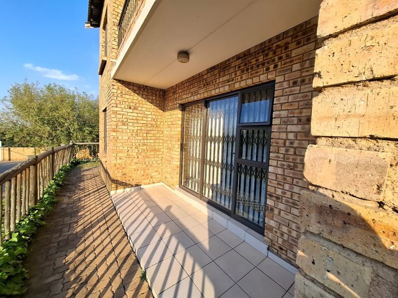 A covered patio area featuring face brick walls, tiled flooring, and a secure sliding glass door with a metal security gate.