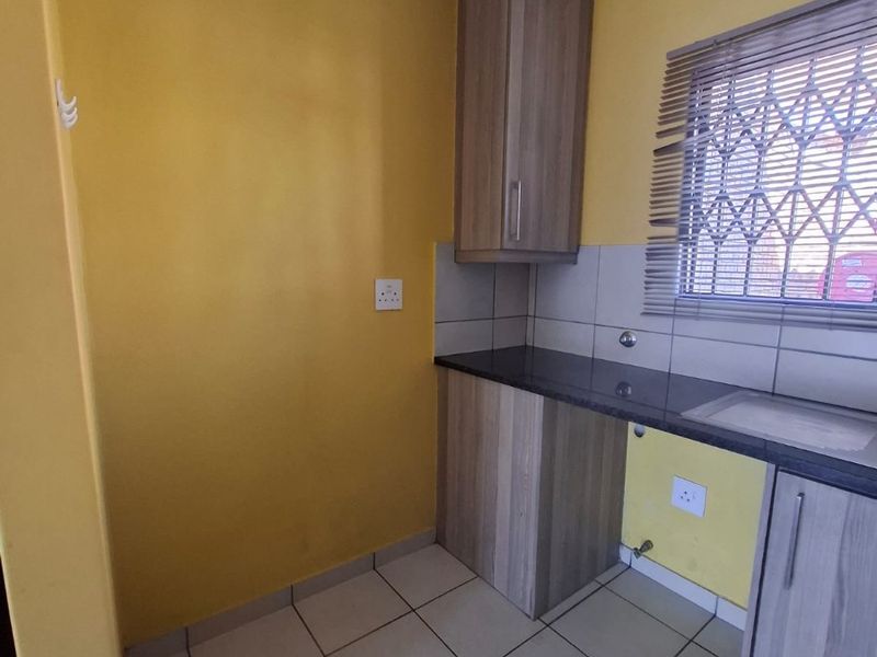A compact kitchen area featuring built-in wood-finish cabinetry, granite countertops, a stainless steel sink, and tiled flooring with a security gate on the window.