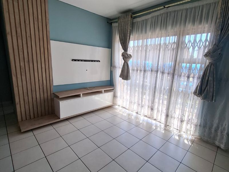 Bright living area featuring tiled flooring, a modern built-in media console with slatted wood accent wall, and access to a balcony through sliding doors.