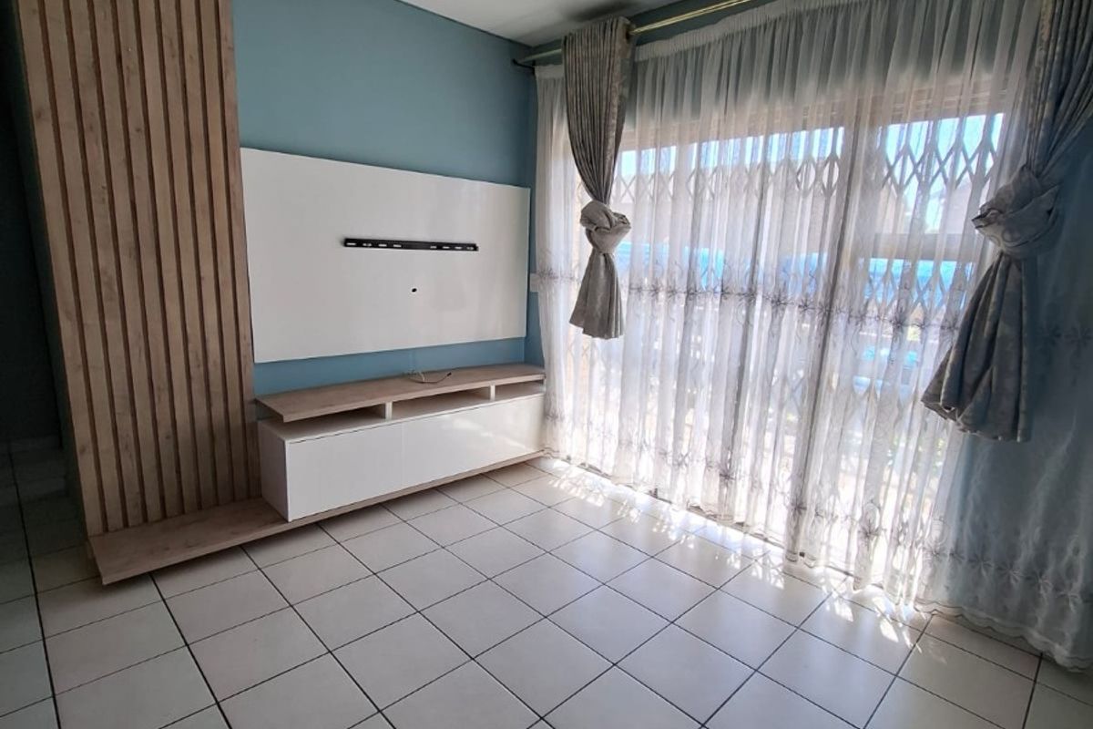 Bright living area featuring tiled flooring, a modern built-in media console with slatted wood accent wall, and access to a balcony through sliding doors.