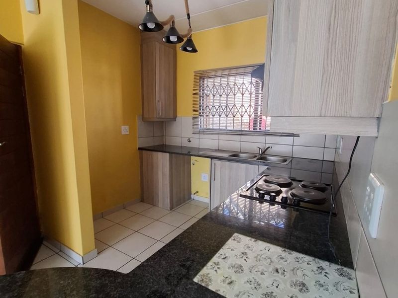 A functional kitchen featuring granite countertops, built-in cabinetry, an electric hob, and a double basin sink with tiled backsplash.