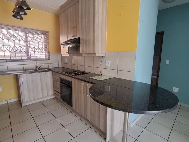 A functional kitchen featuring light wood-finish cabinetry, granite countertops, a built-in oven with gas hob, and tiled flooring.