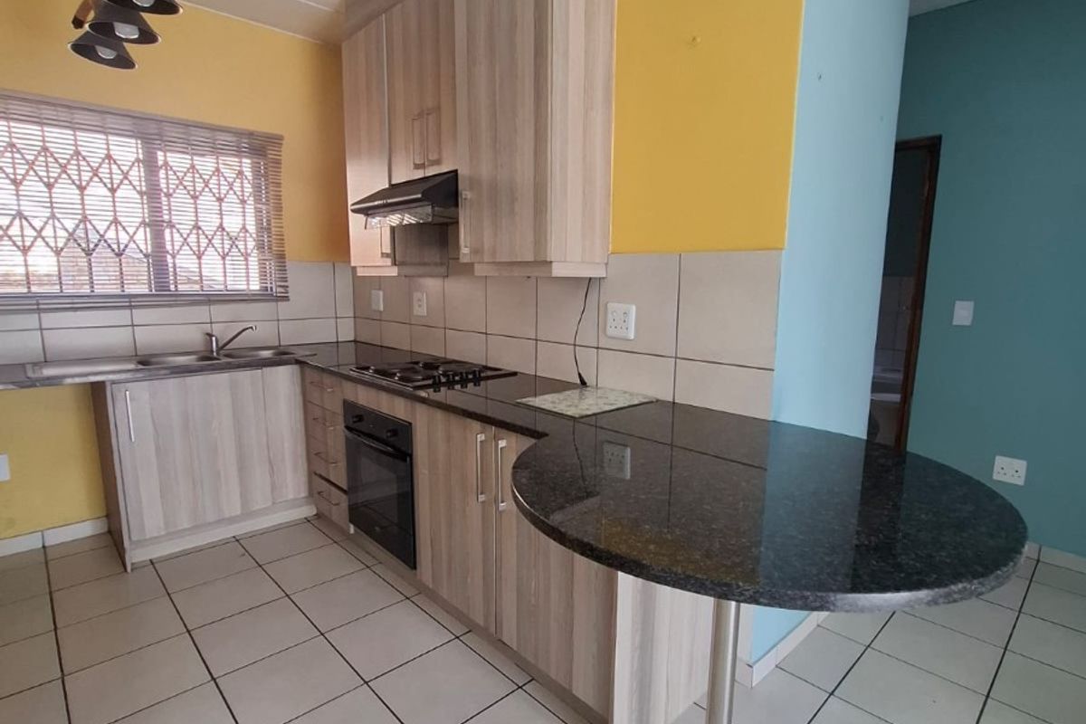 A functional kitchen featuring light wood-finish cabinetry, granite countertops, a built-in oven with gas hob, and tiled flooring.