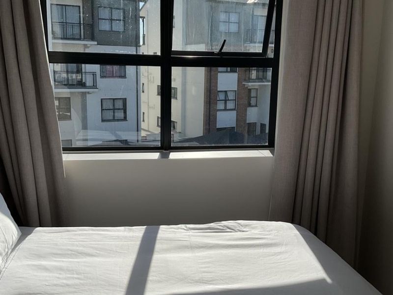 A bright bedroom featuring a modern black aluminium window frame with views of the surrounding apartment complex.