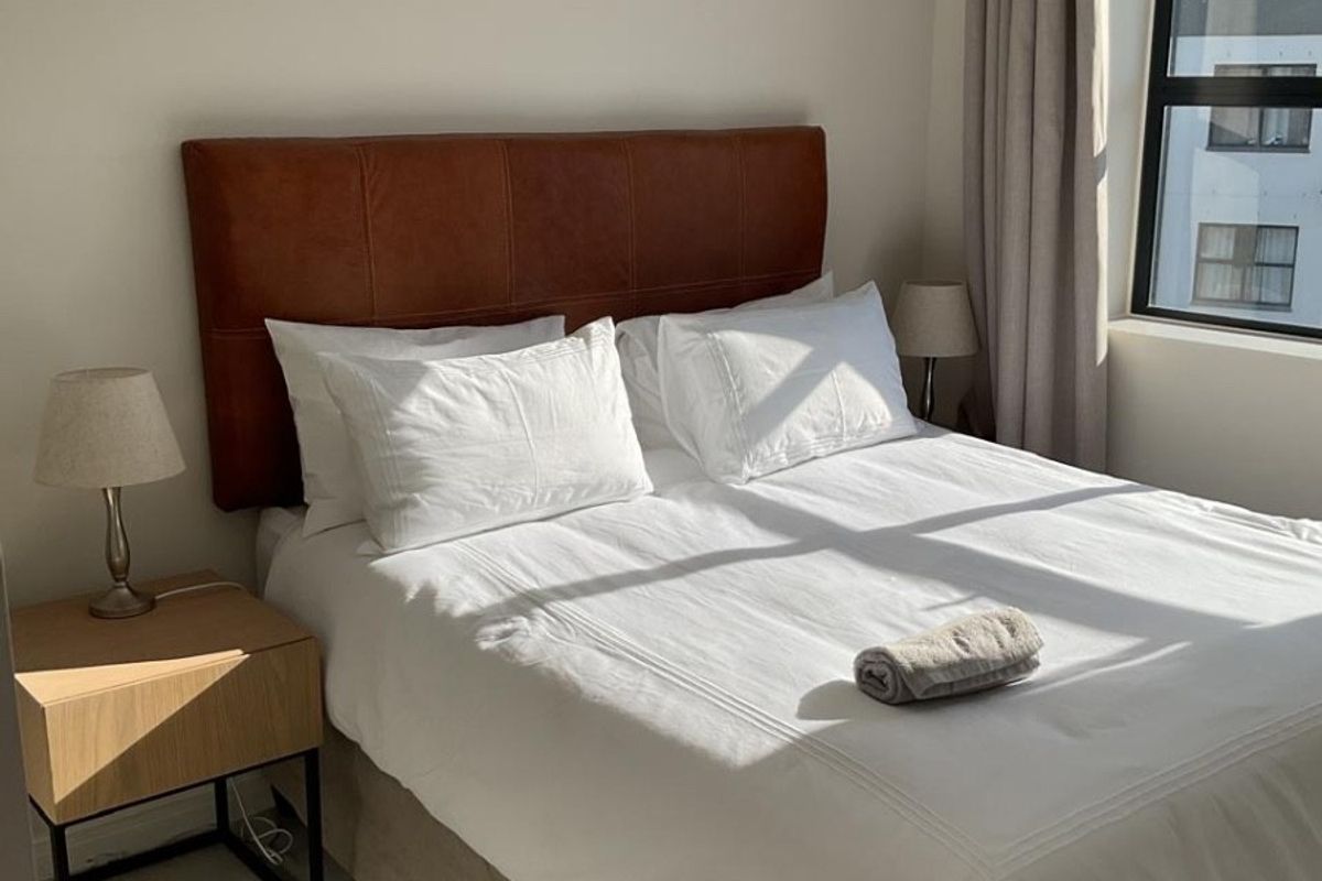 A well-maintained bedroom featuring neutral tiled flooring, modern pendant lighting, and a large window with natural light.