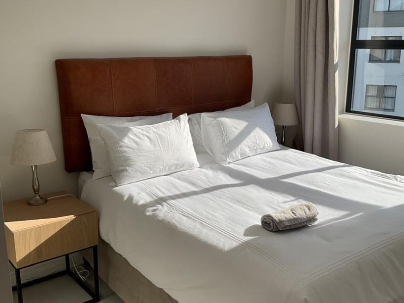 A well-maintained bedroom featuring neutral tiled flooring, modern pendant lighting, and a large window with natural light.