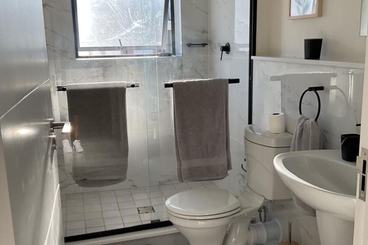 Modern bathroom featuring a walk-in shower with glass screen, pedestal basin, toilet, and elegant marble-look wall tiling.