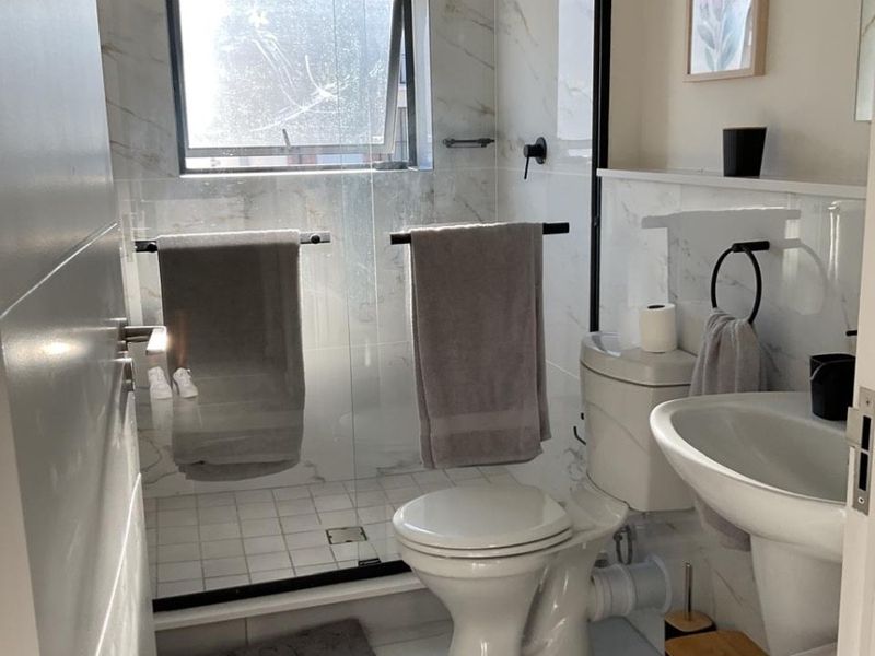 Modern bathroom featuring a walk-in shower with glass screen, pedestal basin, toilet, and elegant marble-look wall tiling.