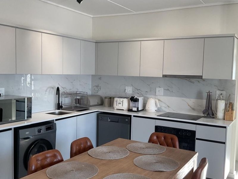 Modern open-plan kitchen featuring sleek white cabinetry, marble-look splashback, integrated appliances, and contemporary track lighting, seamlessly flowing into the dining area.