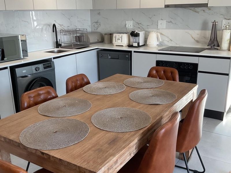 Modern open-plan kitchen featuring sleek white cabinetry, marble-look splashbacks, and integrated appliances, seamlessly flowing into a dining area with tiled flooring.