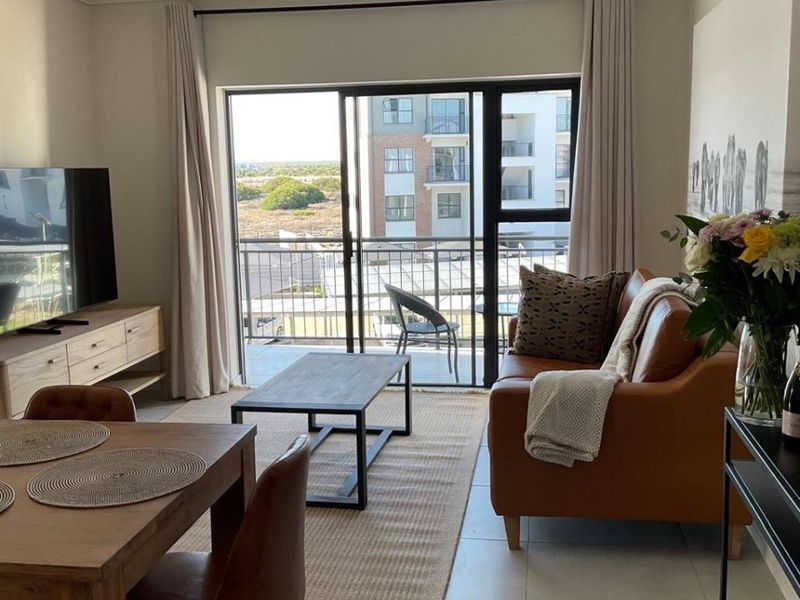 Bright open-plan living area featuring tiled floors, modern track lighting, and a large sliding door providing access to a private balcony.