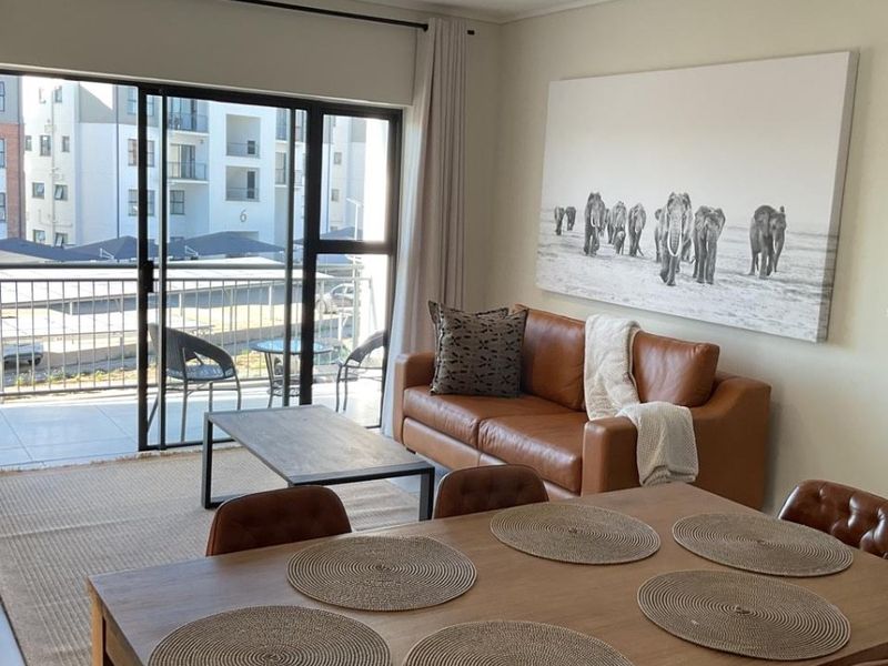 An open-plan living and dining area featuring tiled floors, modern track lighting, and large sliding glass doors leading to a private balcony.