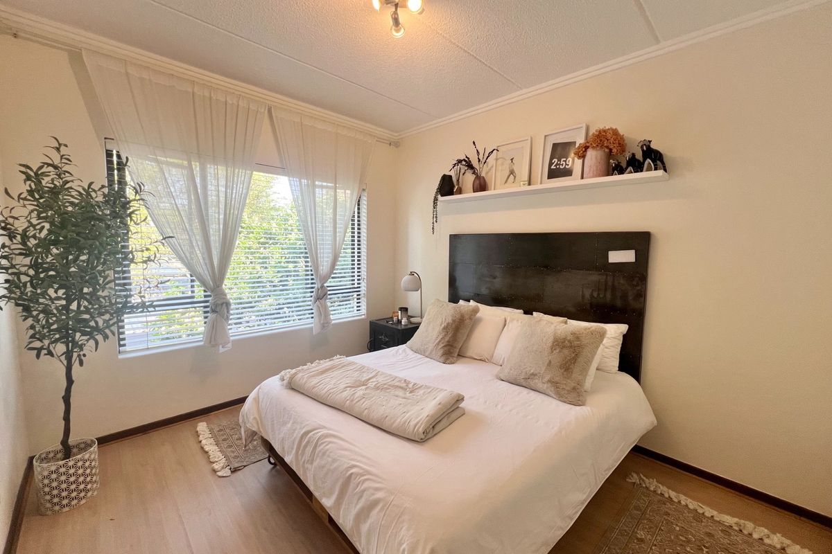 A well-lit bedroom featuring laminate flooring, large windows with venetian blinds, and a neutral color palette.