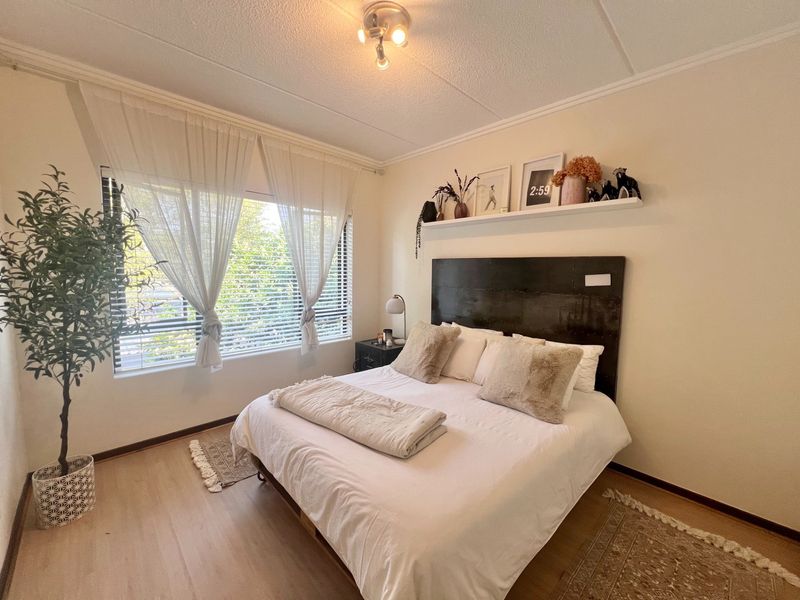 A well-lit bedroom featuring laminate flooring, large windows with venetian blinds, and a neutral color palette.