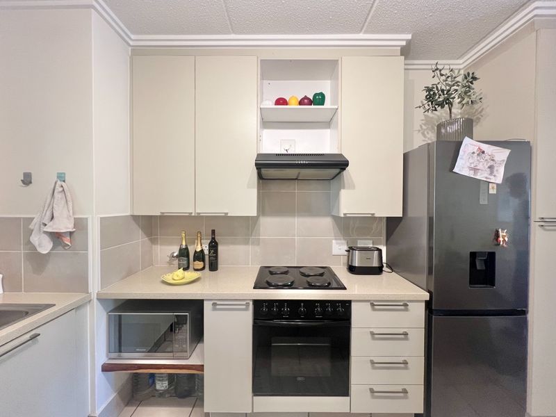 A functional kitchen featuring neutral cabinetry, a tiled backsplash, integrated electric hob and oven, and a dedicated space for a microwave.