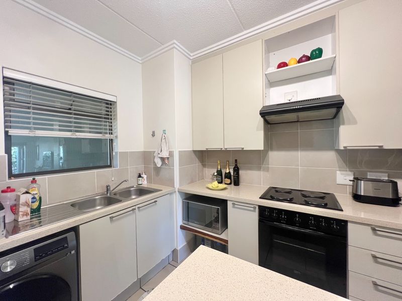 A functional kitchen featuring neutral cabinetry, stone countertops, a built-in oven with electric hob, and a double stainless steel sink with tiled backsplash.