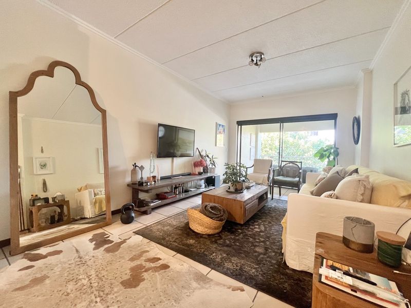A bright living room featuring tiled flooring and a large sliding glass door that provides access to an outdoor balcony area.