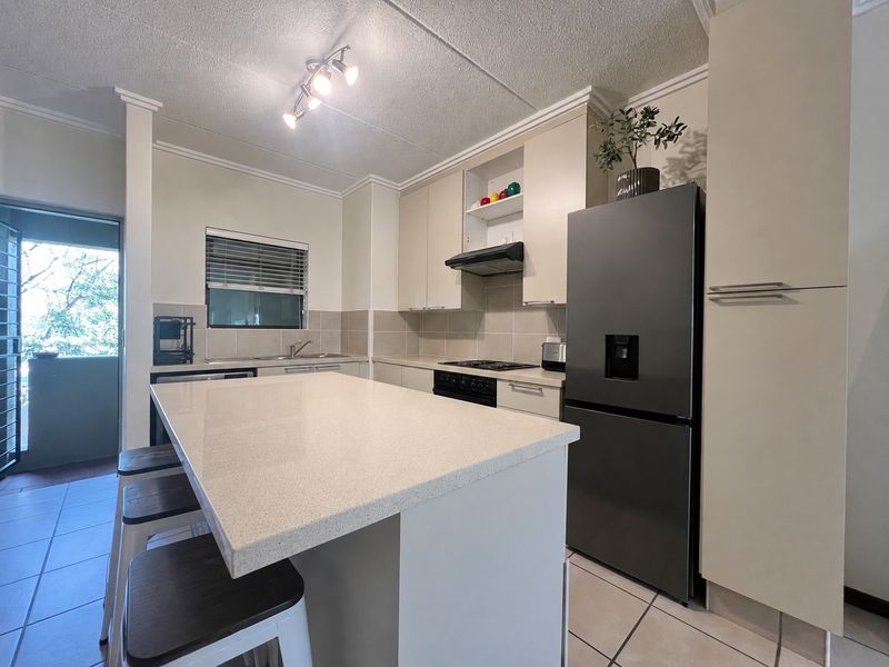 Modern kitchen featuring a central island with quartz countertops, built-in cabinetry, integrated appliances, and tiled flooring, offering a functional and clean cooking space.