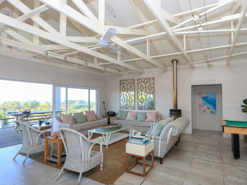 Spacious living area featuring exposed timber roof trusses, a freestanding fireplace, and large sliding glass doors opening onto an outdoor deck with scenic views.