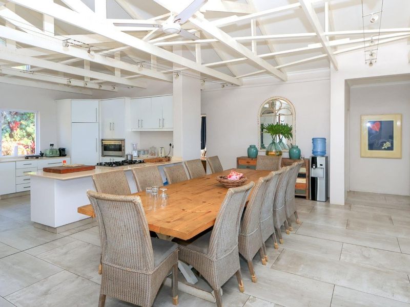Spacious open-plan kitchen and dining area featuring exposed white timber ceiling beams, modern cabinetry, a central kitchen island, and neutral tiled flooring throughout.