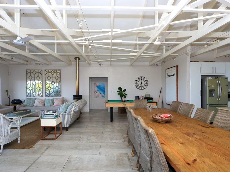 Spacious open-plan living and dining area featuring high exposed timber roof trusses, tiled flooring, and a central freestanding fireplace.