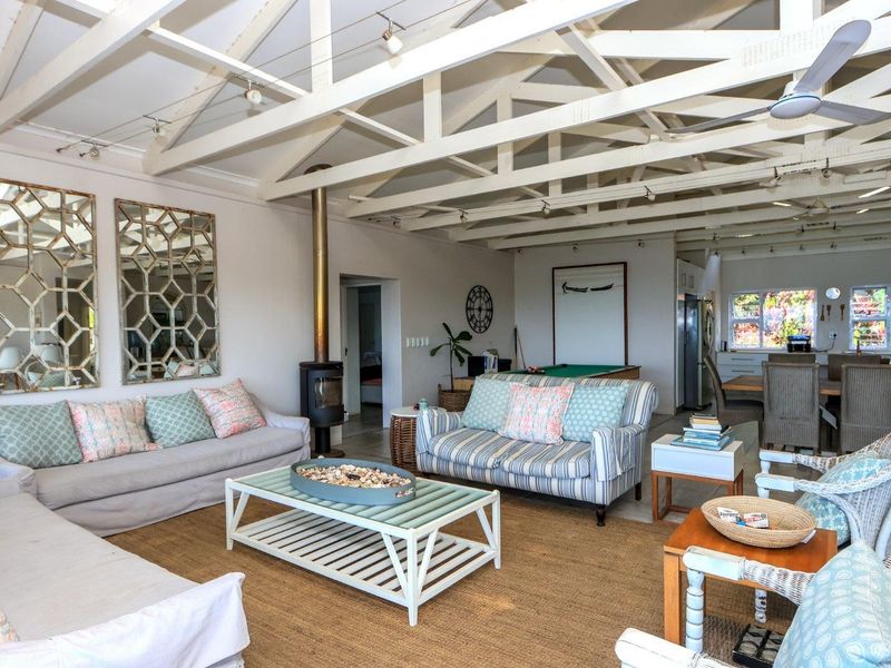 Spacious open-plan living and dining area featuring high vaulted ceilings with exposed timber trusses, a central fireplace, and integrated track lighting.