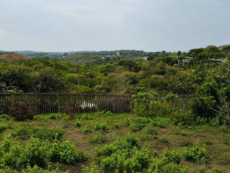 A scenic view overlooking a lush green valley and surrounding landscape, featuring a wooden boundary fence in the foreground.