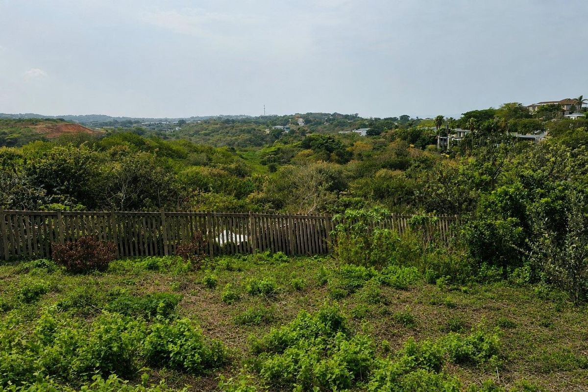 A scenic view overlooking a lush green valley and surrounding landscape, featuring a wooden boundary fence in the foreground.