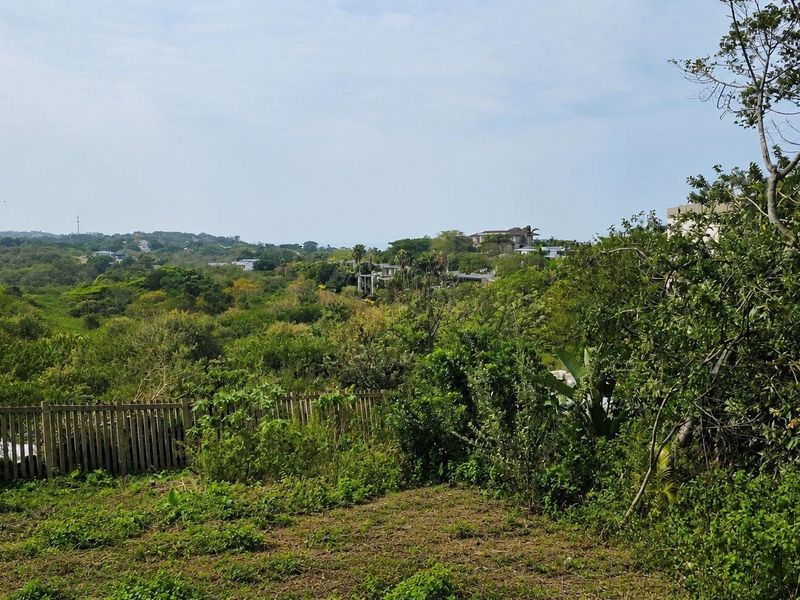 A scenic view overlooking a lush green landscape with established vegetation and a wooden boundary fence on the residential property.