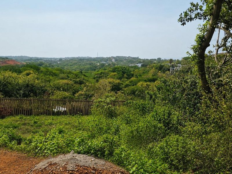 A scenic view overlooking a lush, green landscape with a wooden boundary fence in the foreground.