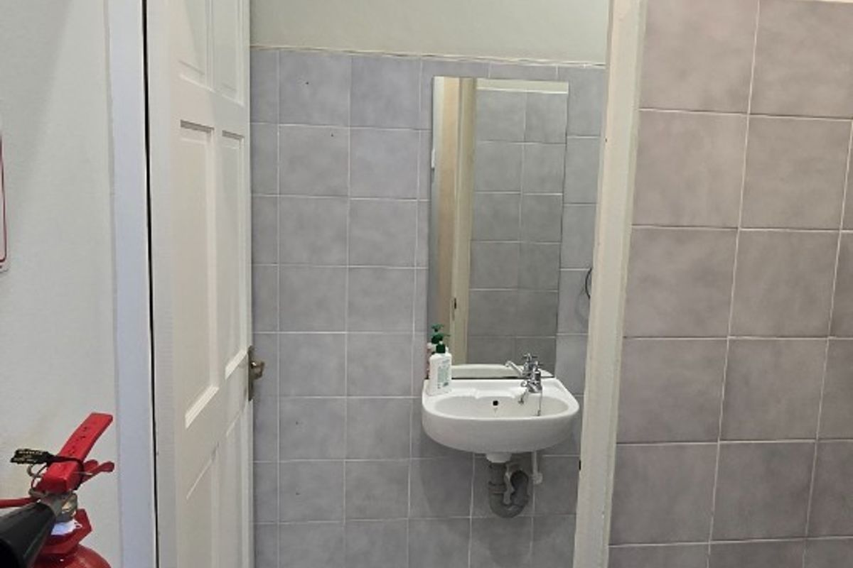 A compact bathroom featuring a wall-mounted basin, tiled walls and flooring, and a wall-mounted mirror.