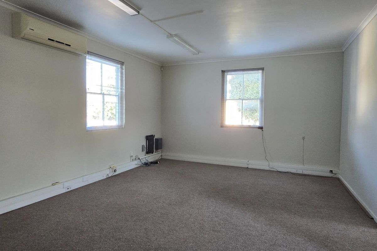 A spacious, empty bedroom featuring neutral walls, carpet flooring, a split-system air conditioner, and natural light from multiple sash windows.