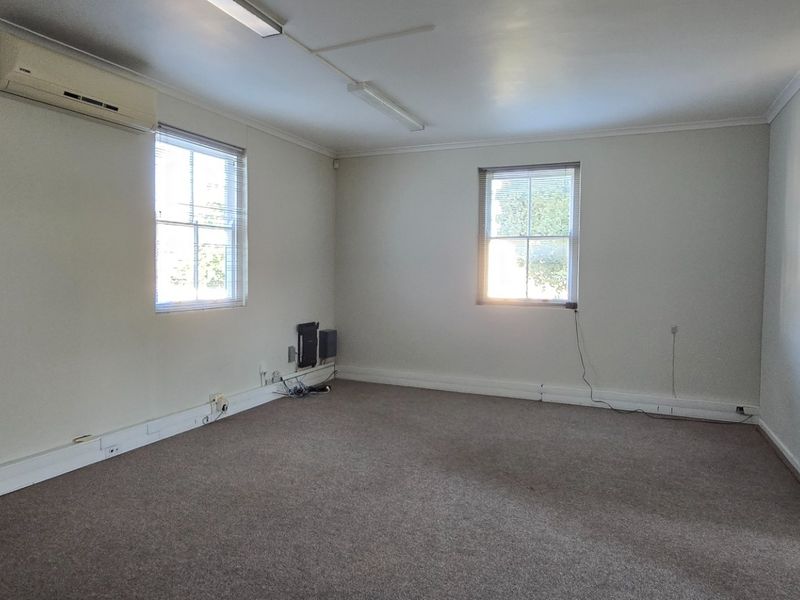 A spacious, empty bedroom featuring neutral walls, carpet flooring, a split-system air conditioner, and natural light from multiple sash windows.